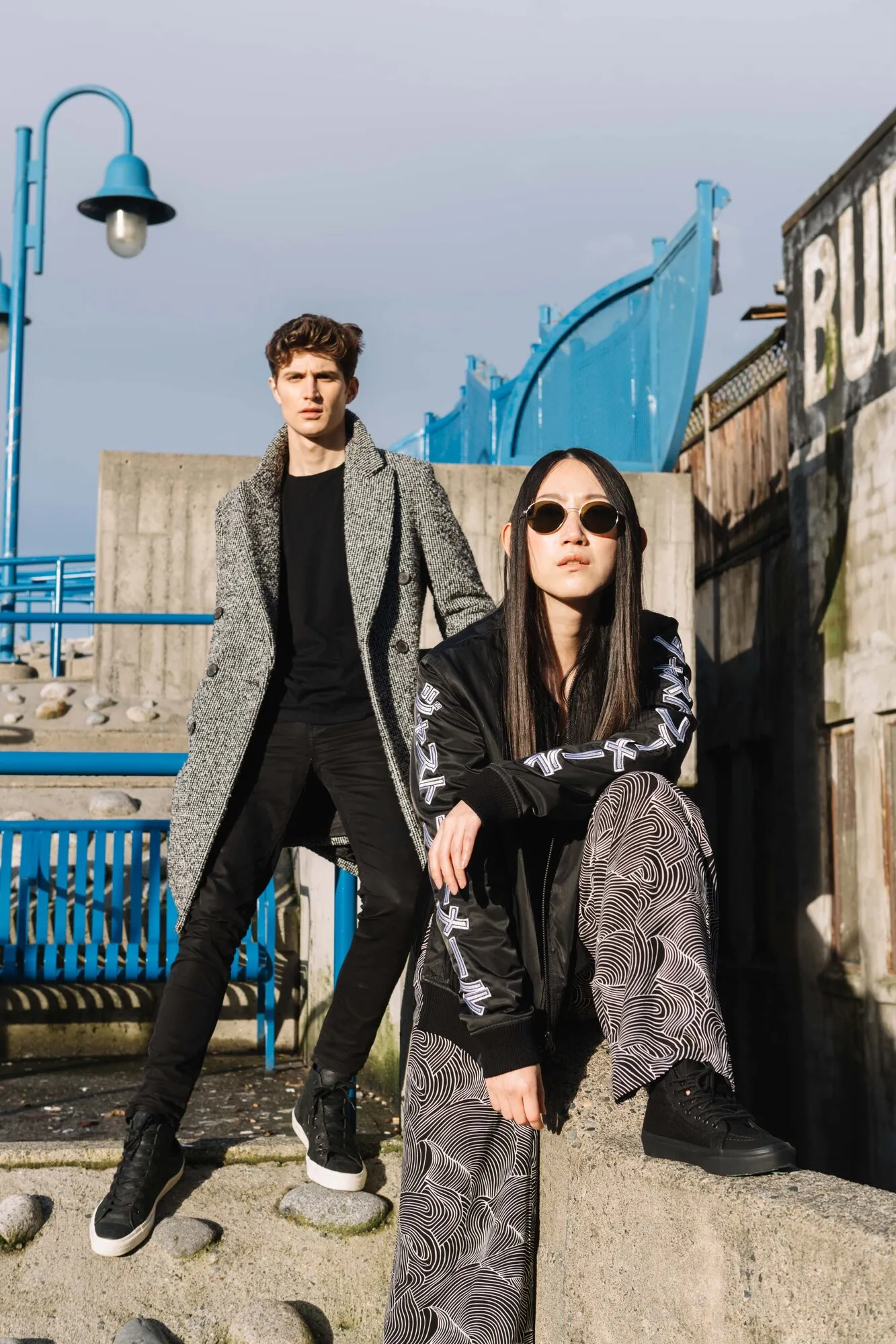 Editorial portrait of two models posed against a blue playground structure by the waterfront