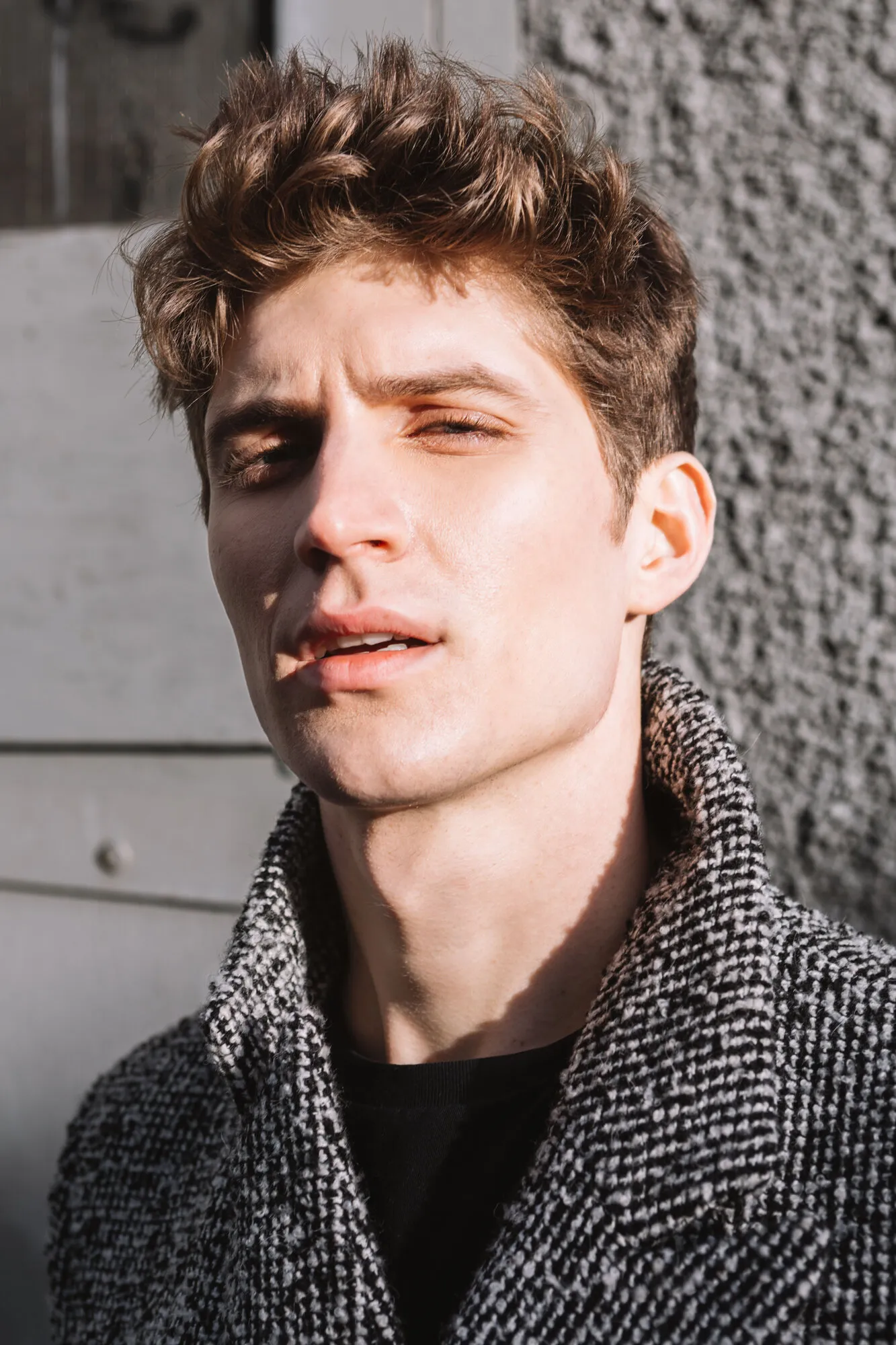 Sunlit portrait of a model in a grey tweed coat against a concrete wall