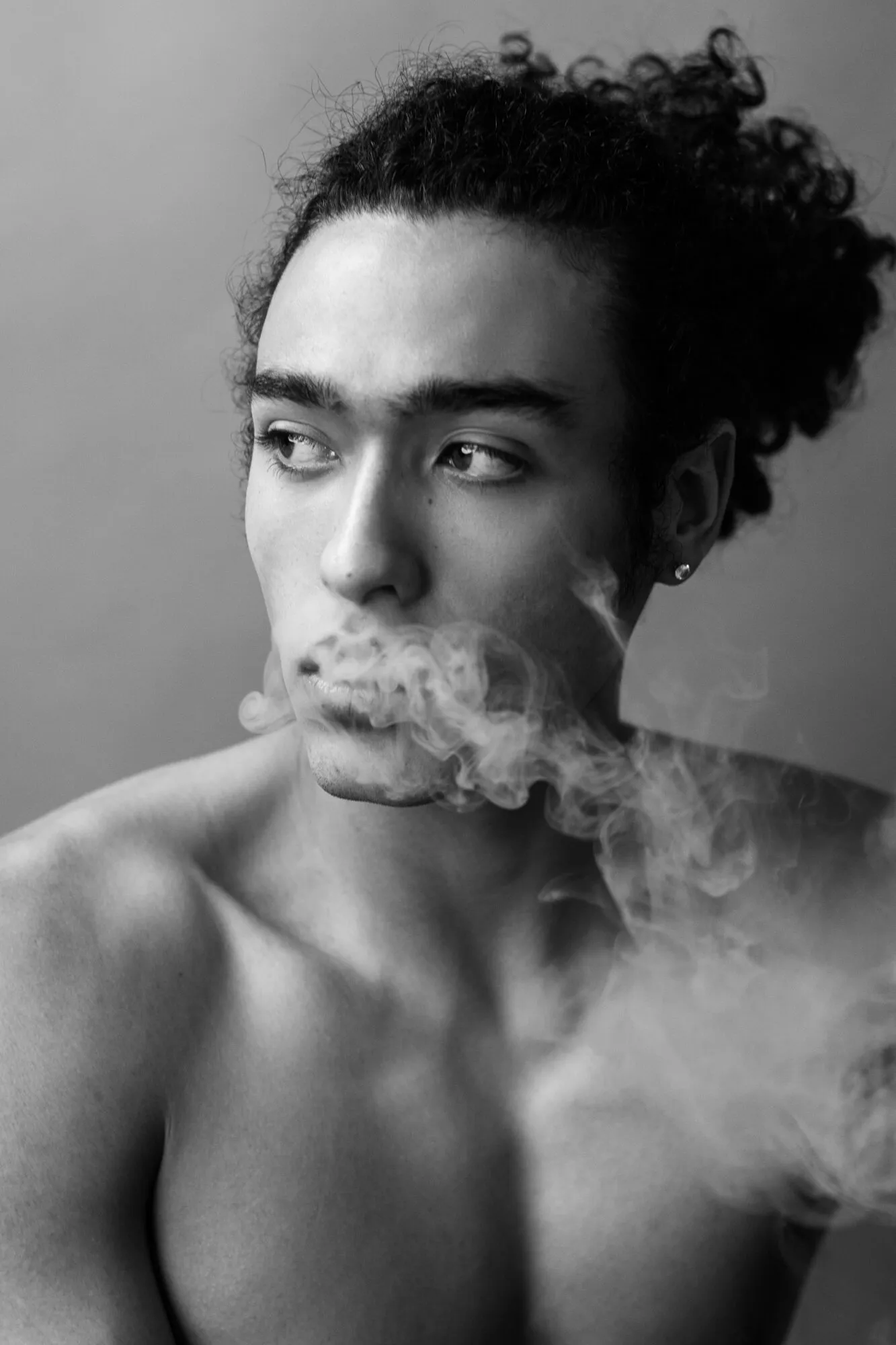 Black and white portrait of a model exhaling smoke, hair tied up