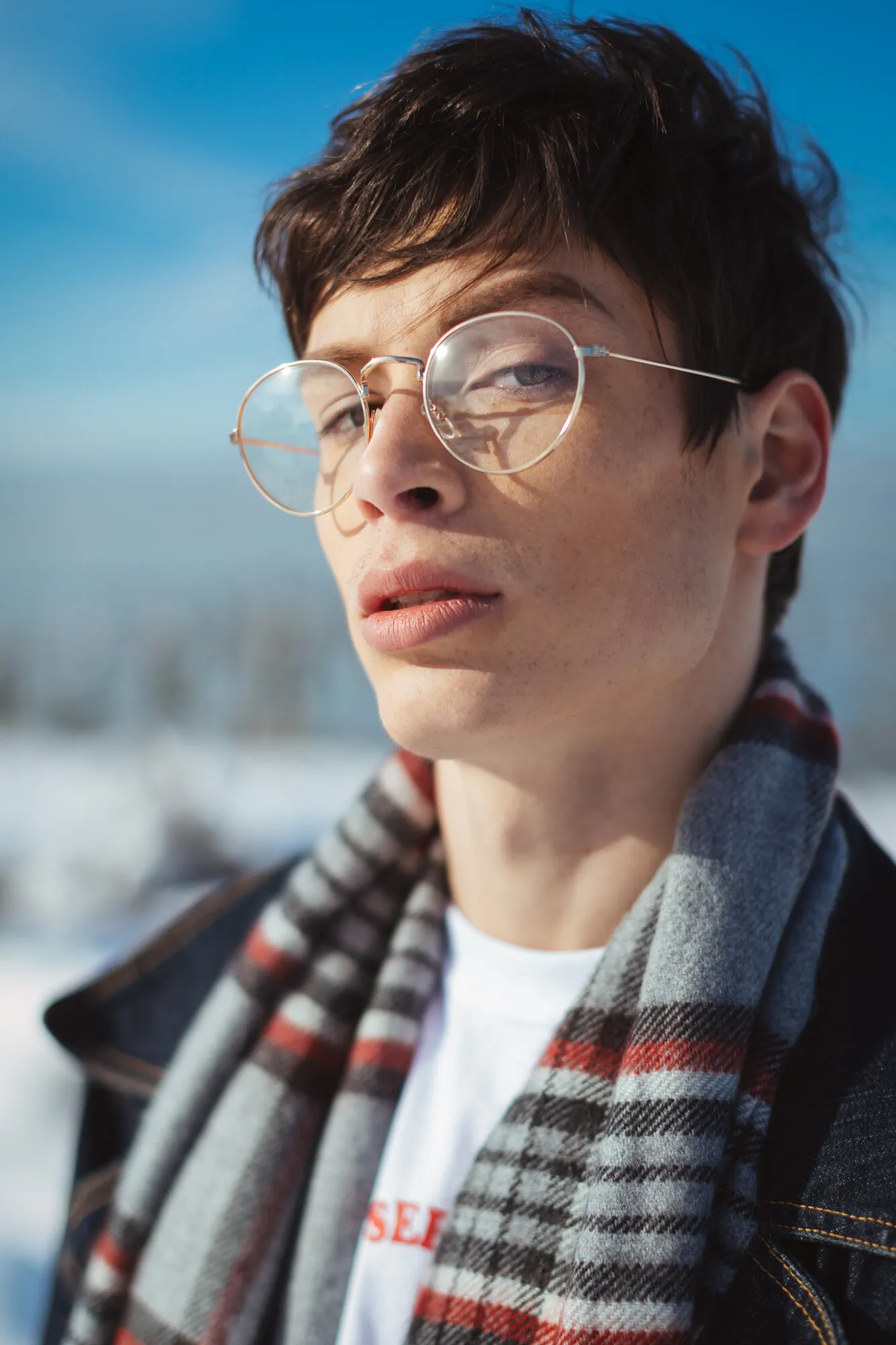 Portrait of a model in round glasses and a plaid scarf gazing upward against a blue sky