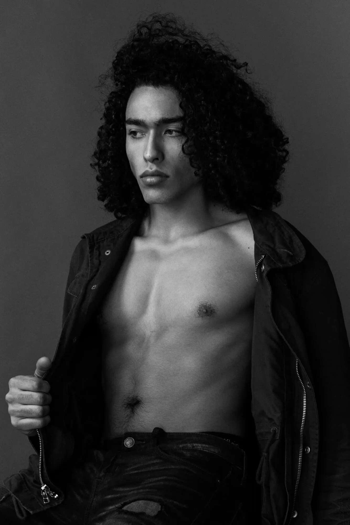 Black and white studio portrait of a model with long curls, jacket open