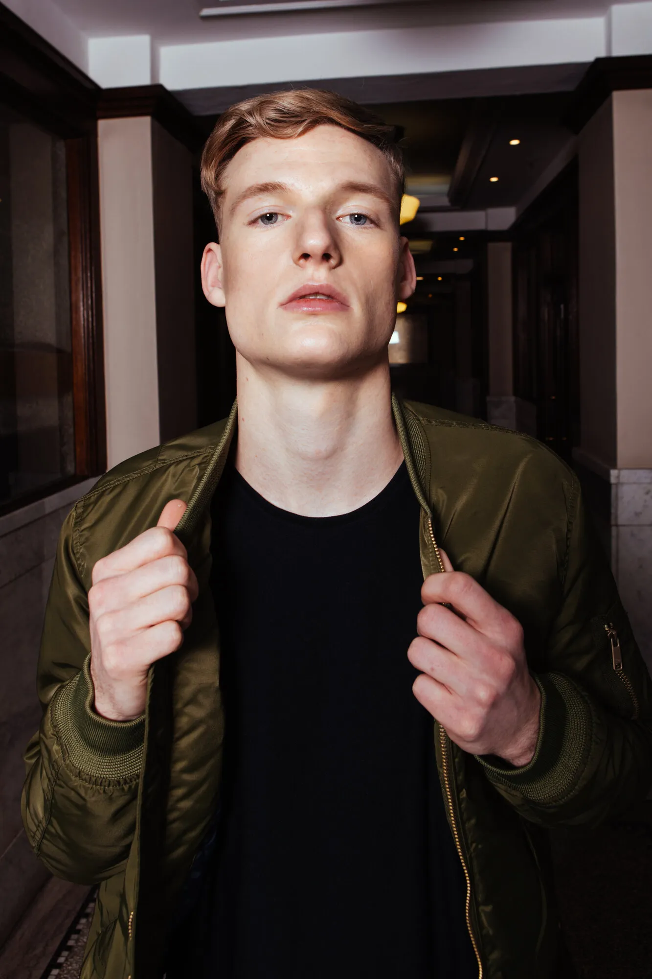 Portrait of a red-haired model gripping the collar of an olive bomber jacket