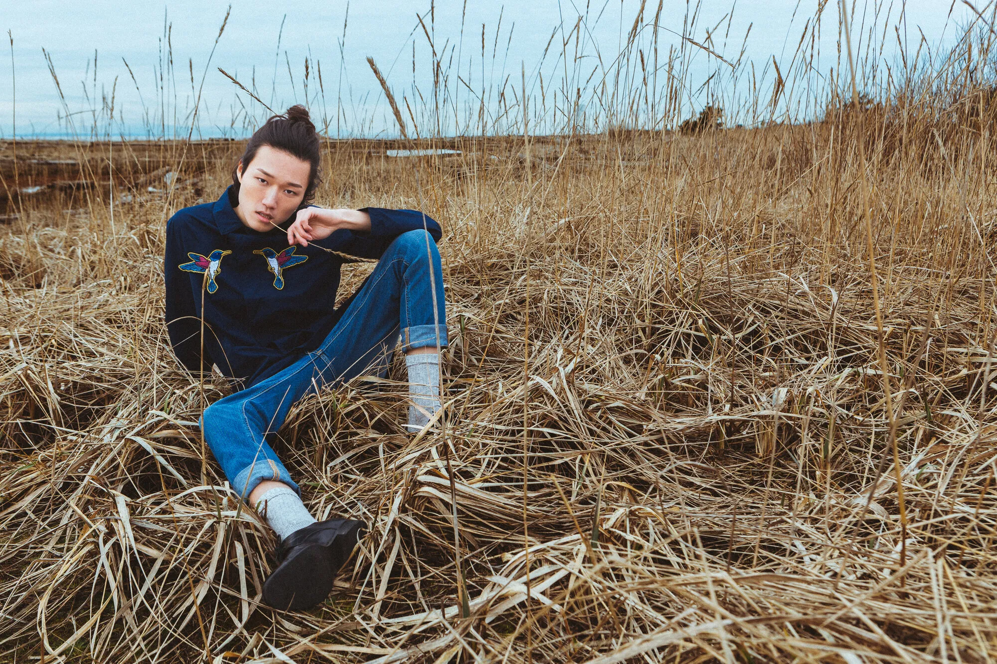 Model reclining in tall dried grass in denim, photographed for The Boundary
